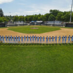 Elevated drone shot of the 2023 Redding Colt 45s squad standing in a line, along the base path behind second base, with the pitcher's mound, home plate and the stands in the background.